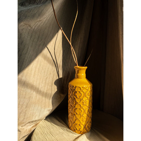 A mustard yellow ceramic vase with an embossed quatrefoil pattern, shown with and without dried branches inside.
