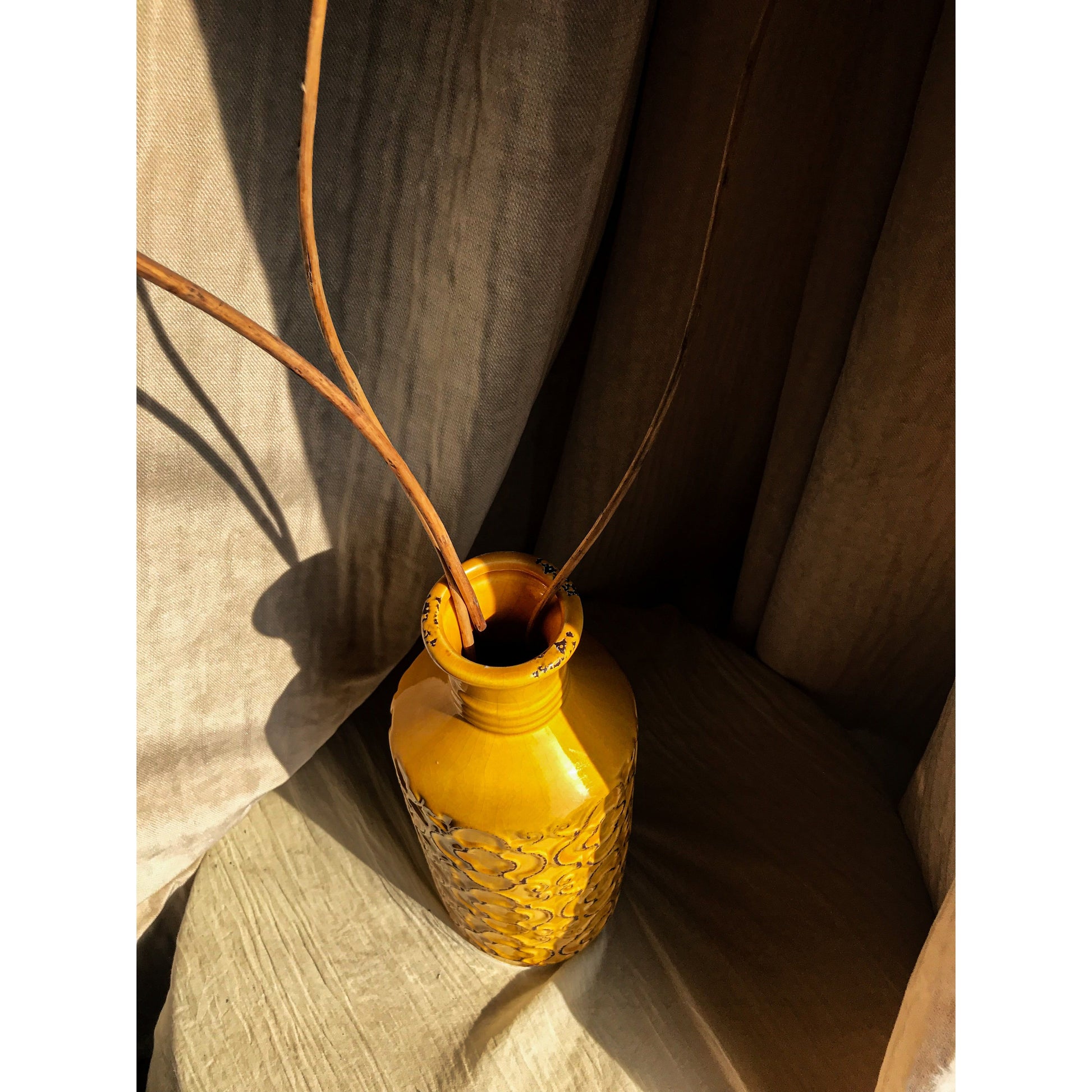 A mustard yellow ceramic vase with an embossed quatrefoil pattern, shown with and without dried branches inside.