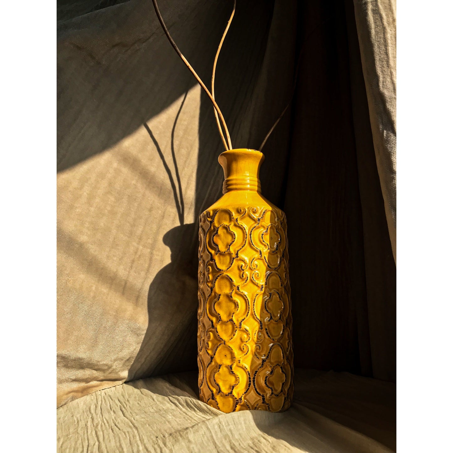 A mustard yellow ceramic vase with an embossed quatrefoil pattern, shown with and without dried branches inside.