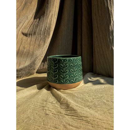 A green ceramic planter with an embossed leaf pattern on the upper portion and a natural, unglazed ceramic base.