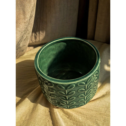 A green ceramic planter with an embossed leaf pattern on the upper portion and a natural, unglazed ceramic base.