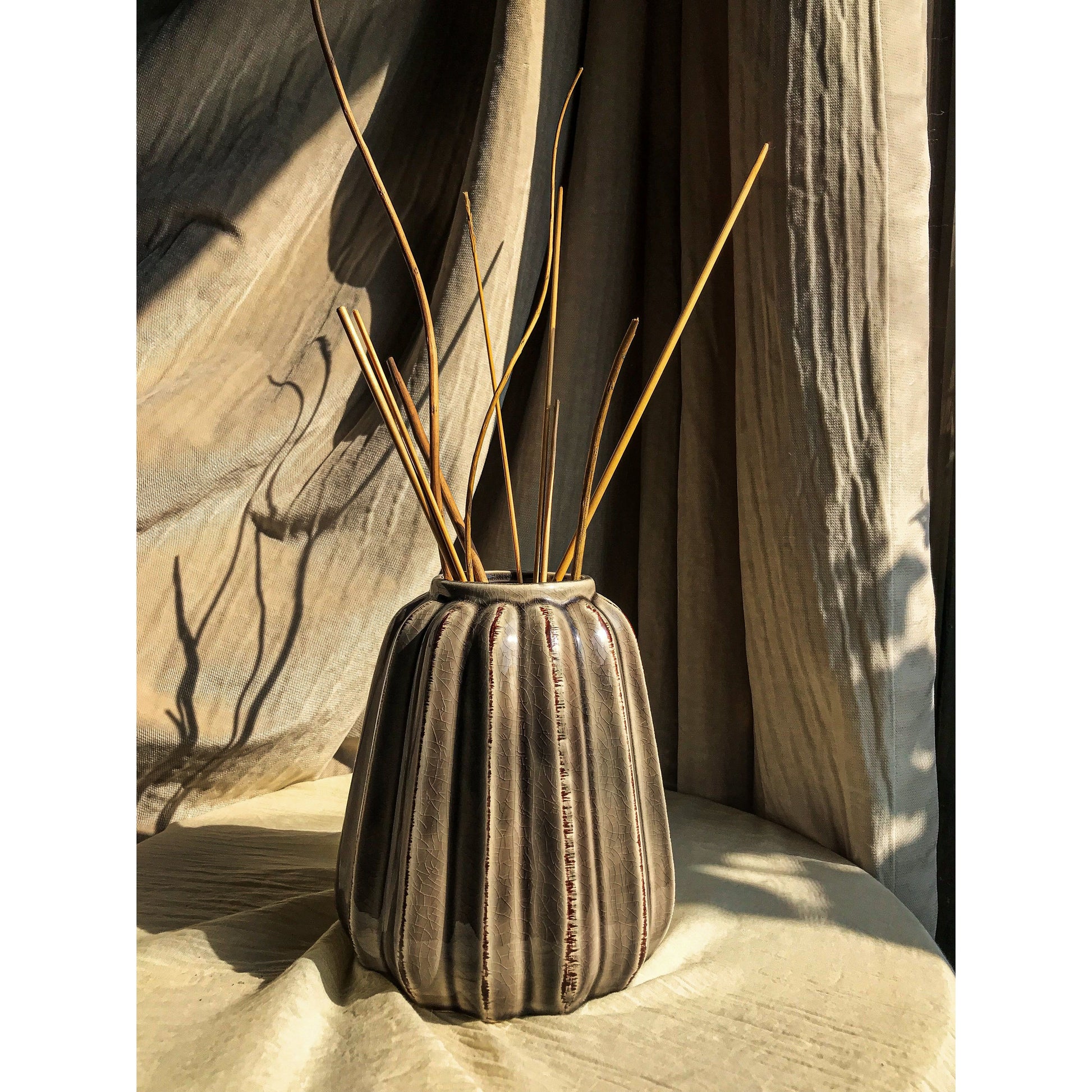 A grey ceramic vase with vertical fluting and a crackled glaze, shown empty and with dried branches inside.