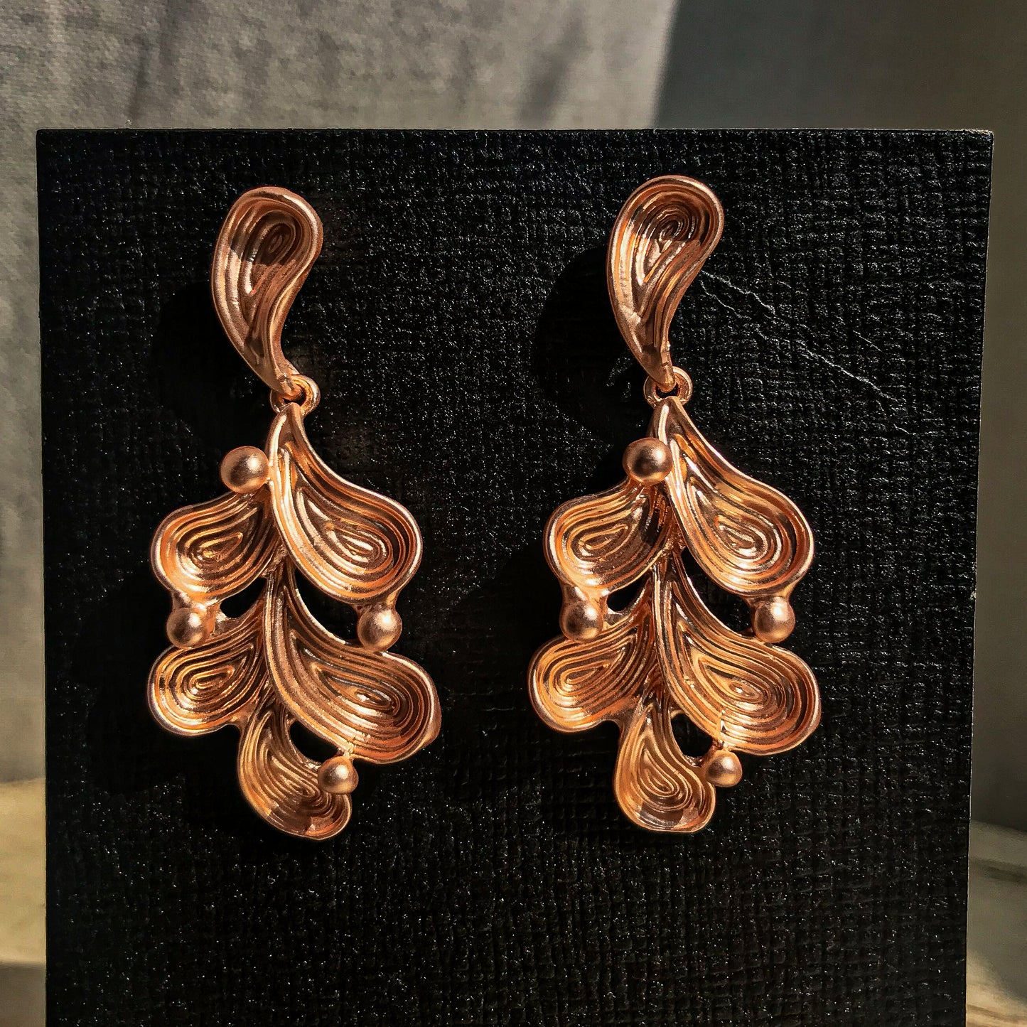 Two abstract drop earrings with swirling lines and small round accents, shown in silver, gold, rose gold, and black variations.