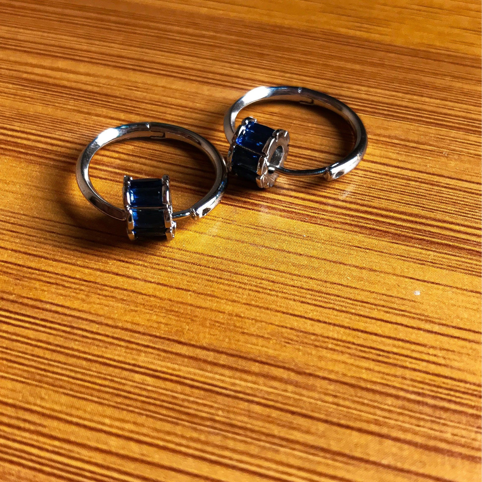 Two small silver hoop earrings, each with a cluster of rectangular blue stones on the front, resting on a wooden surface.