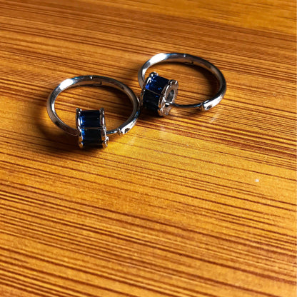 Two small silver hoop earrings, each with a cluster of rectangular blue stones on the front, resting on a wooden surface.