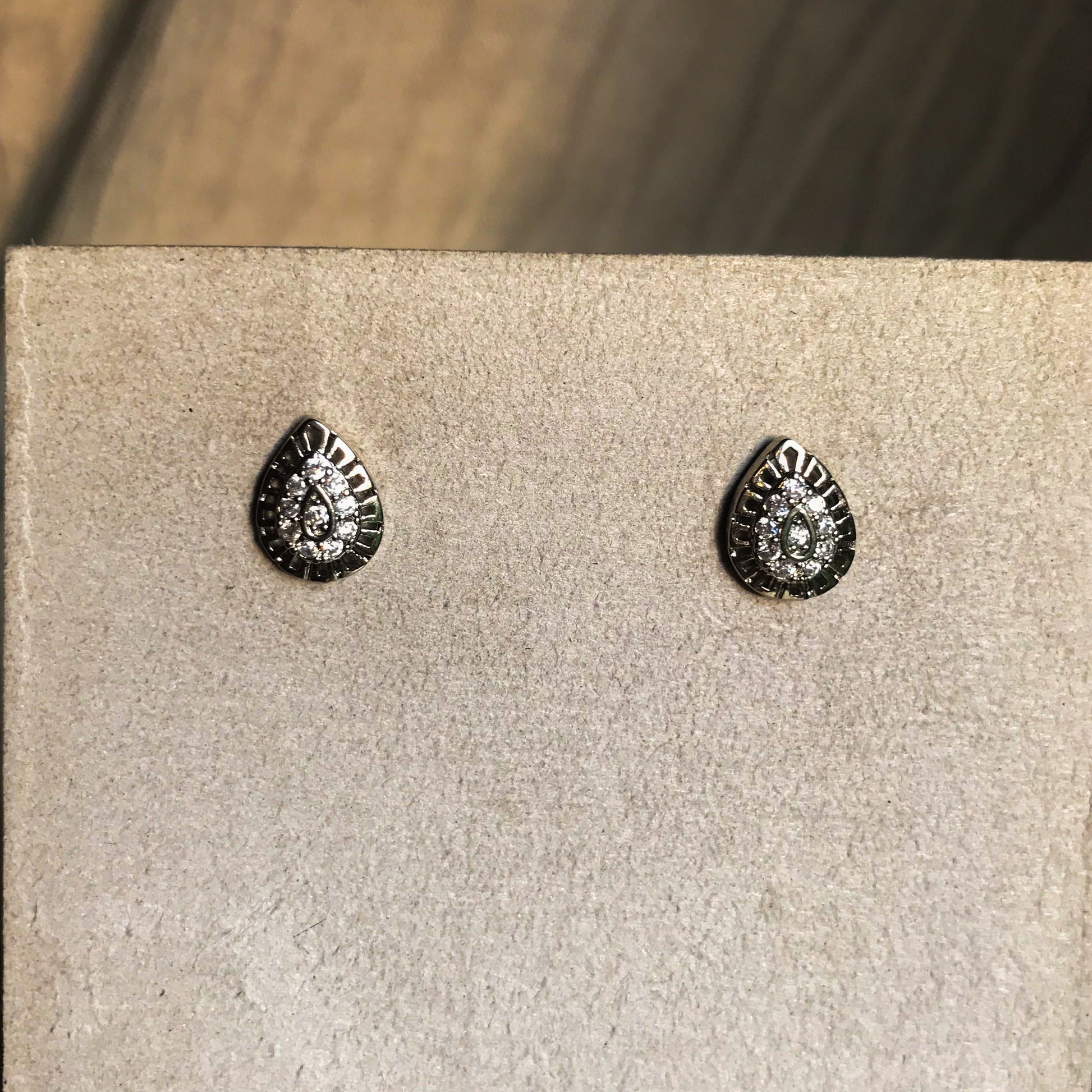 Silver teardrop-shaped stud earrings with crystal accents on a beige display stand