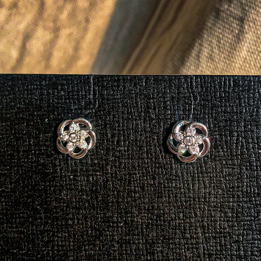 Two small, silver flower-shaped stud earrings with sparkling clear stones in the center, displayed on a black earring card.
