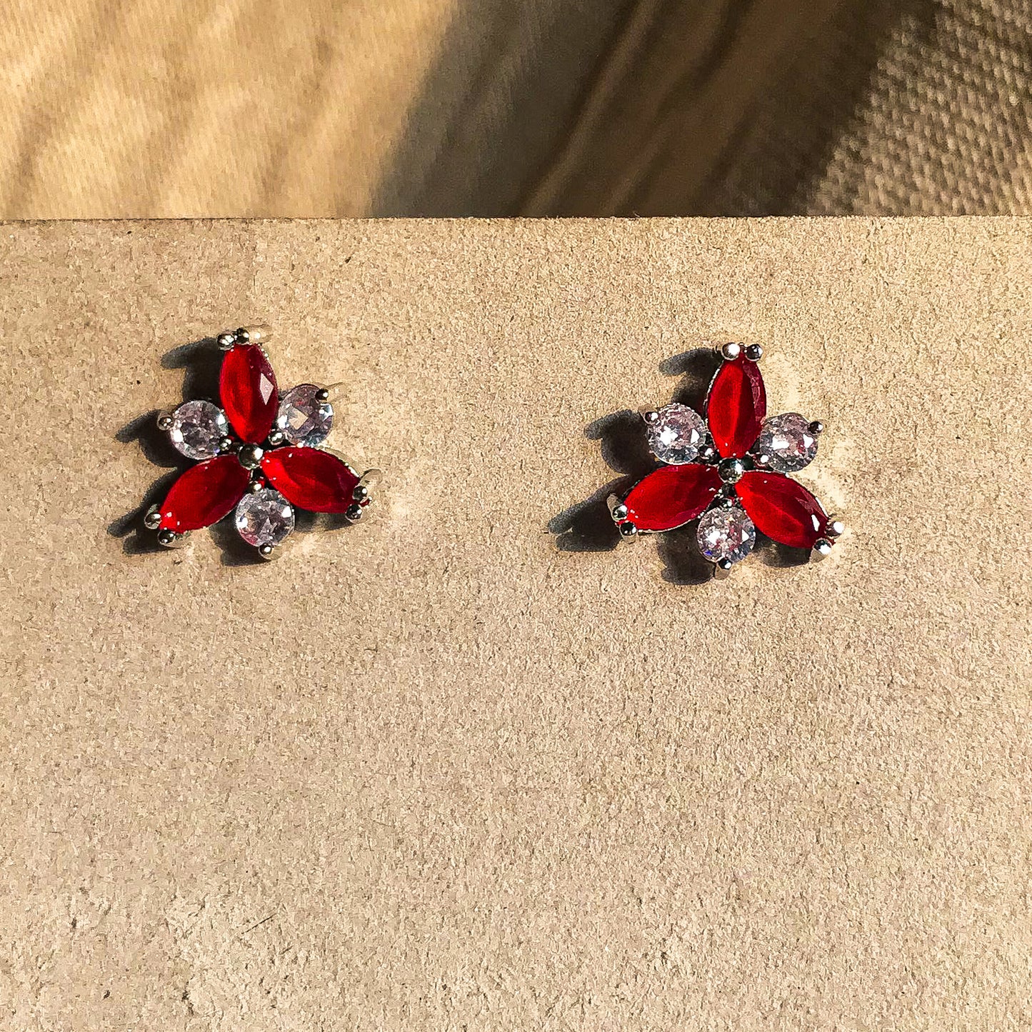 Two small, silver flower-shaped stud earrings set with clear, sparkling stones, displayed on a black earring card.