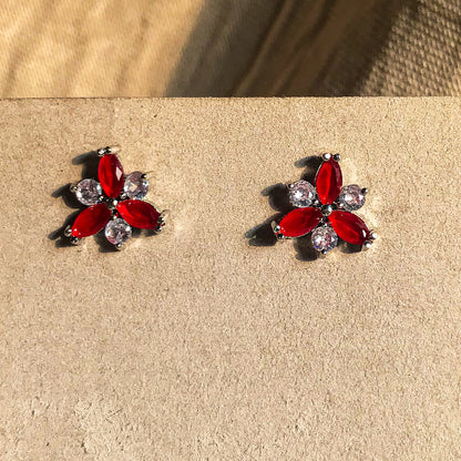 Two small, silver flower-shaped stud earrings set with clear, sparkling stones, displayed on a black earring card.