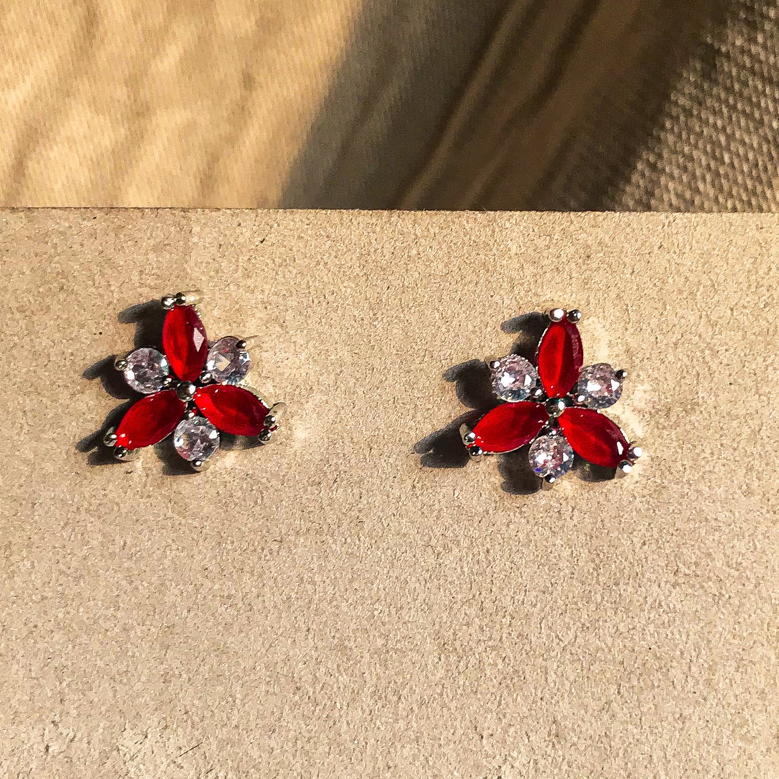Two small, silver flower-shaped stud earrings set with clear, sparkling stones, displayed on a black earring card.