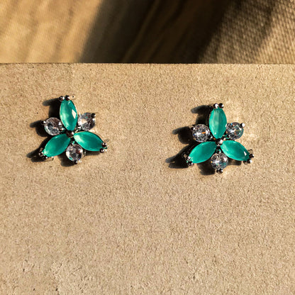 Two small, silver flower-shaped stud earrings set with clear, sparkling stones, displayed on a black earring card.