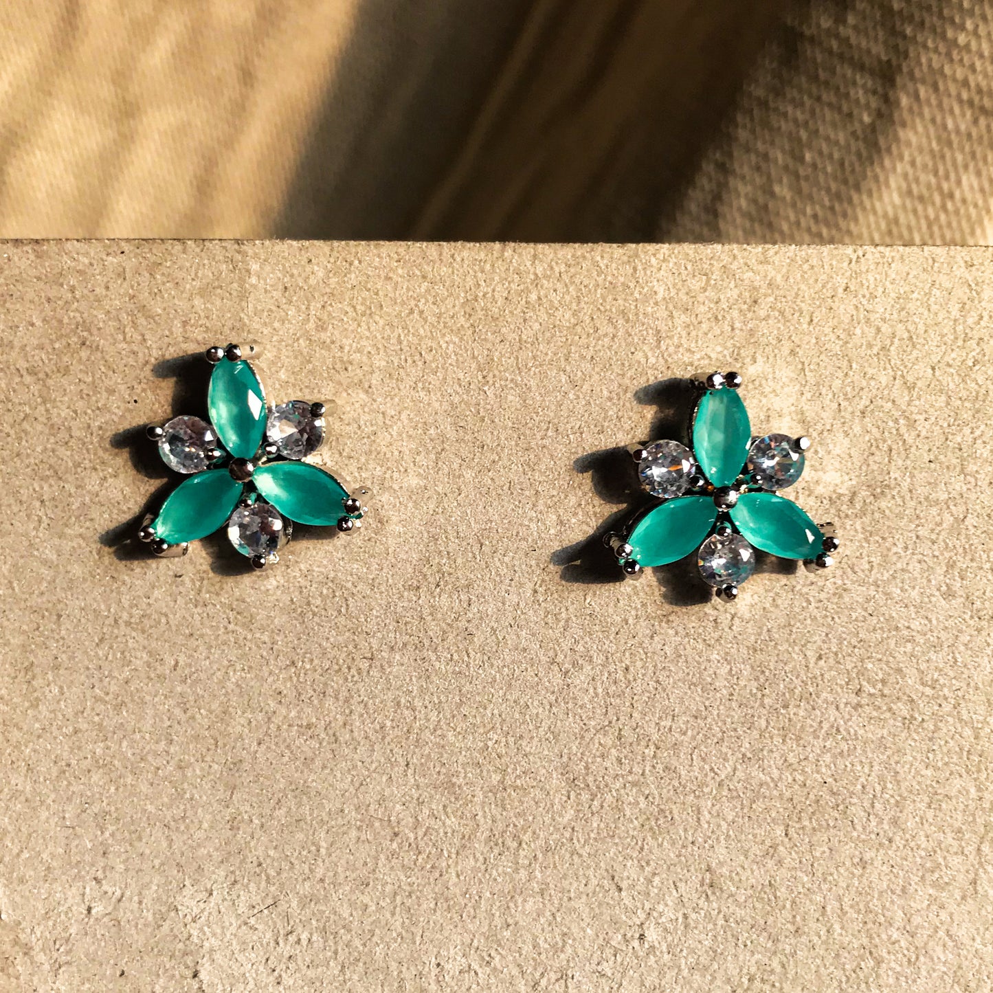 Two small, silver flower-shaped stud earrings set with clear, sparkling stones, displayed on a black earring card.