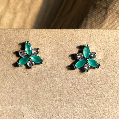 Two small, silver flower-shaped stud earrings set with clear, sparkling stones, displayed on a black earring card.