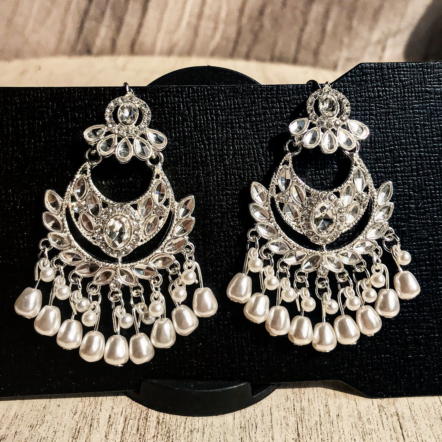 Two ornate silver-tone chandelier earrings with multiple clear crystals and cascading strands of white pearls, displayed on a black earring card.