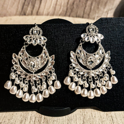Two ornate silver-tone chandelier earrings with multiple clear crystals and cascading strands of white pearls, displayed on a black earring card.