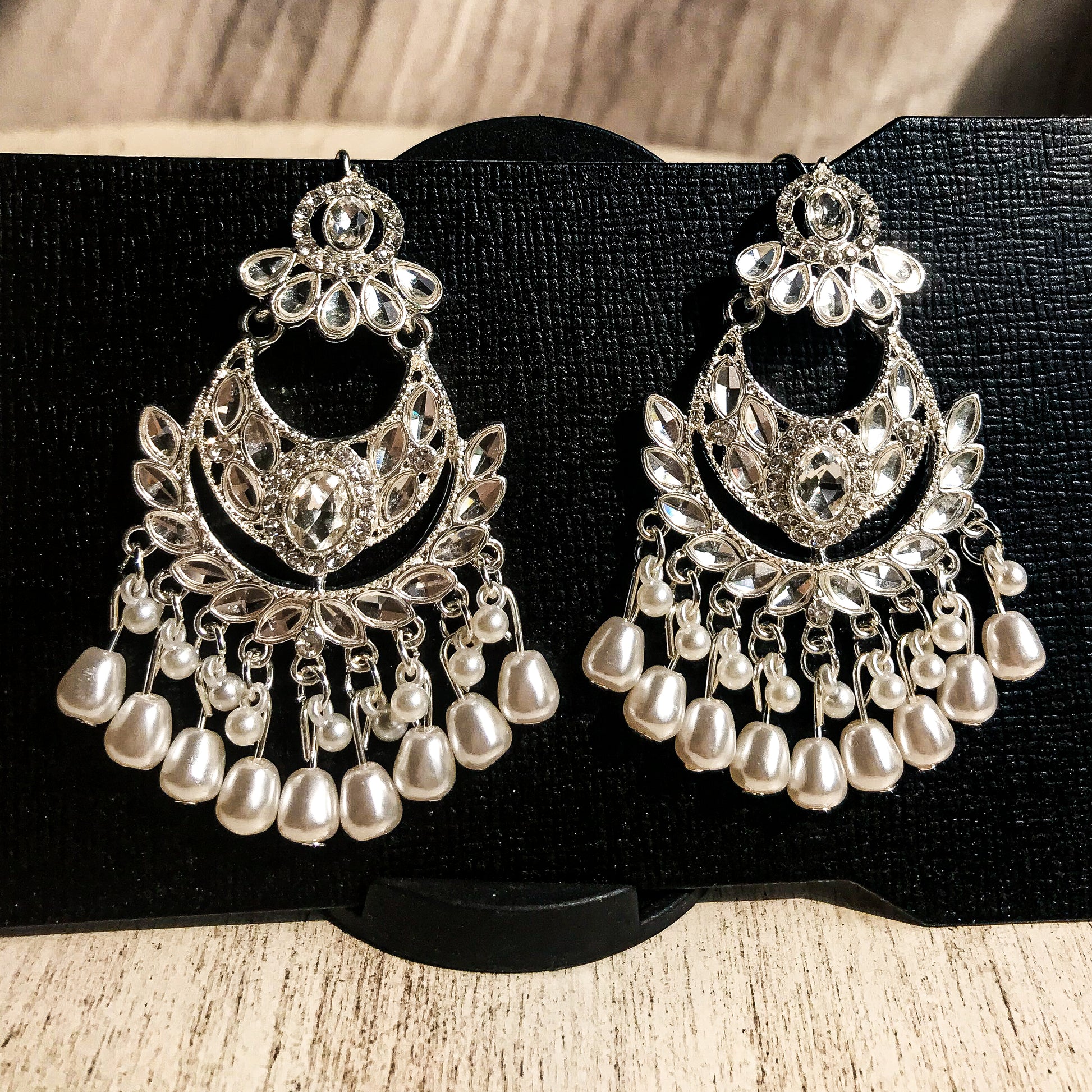 Two ornate silver-tone chandelier earrings with multiple clear crystals and cascading strands of white pearls, displayed on a black earring card.