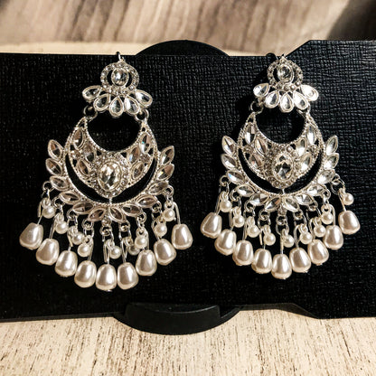 Two ornate silver-tone chandelier earrings with multiple clear crystals and cascading strands of white pearls, displayed on a black earring card.