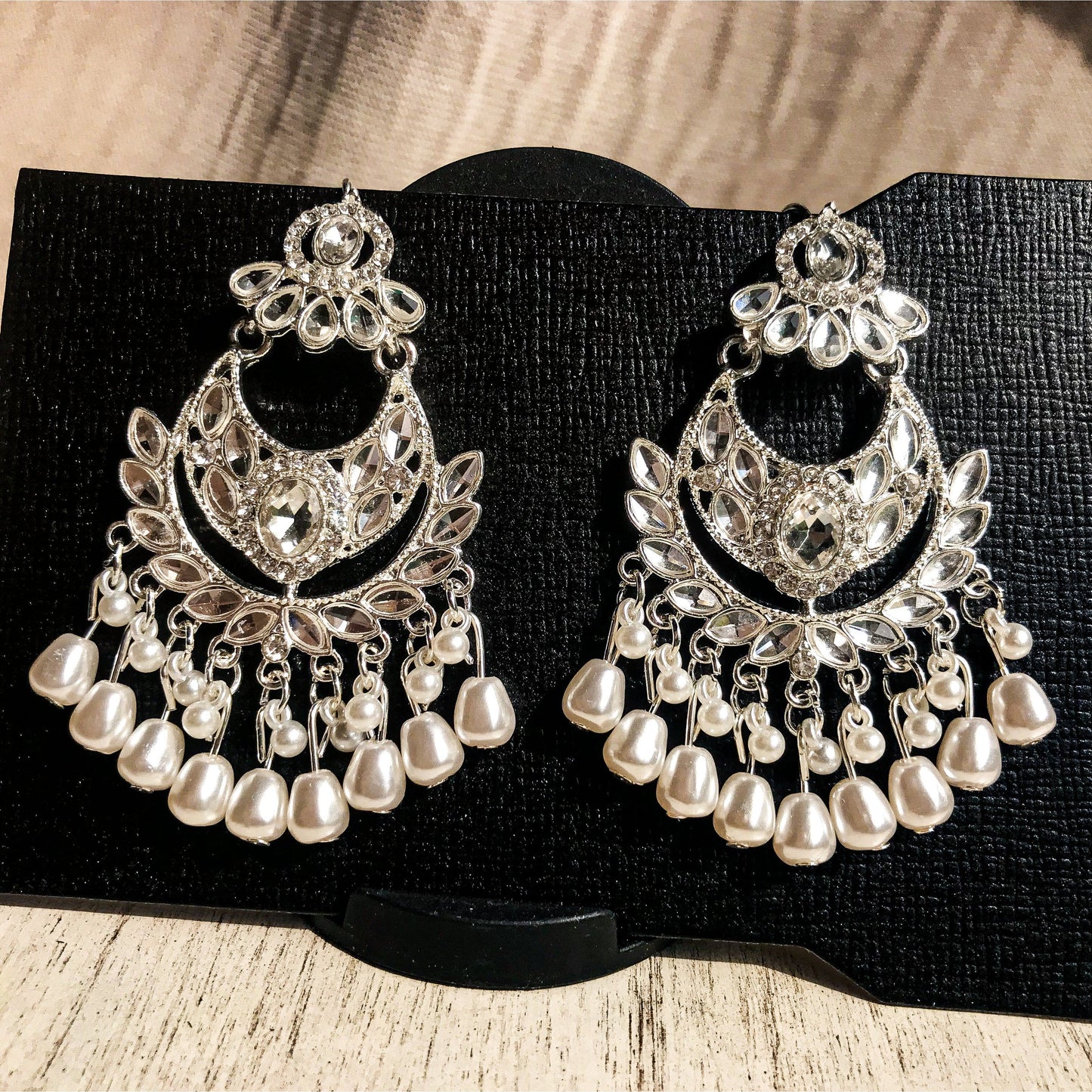 Two ornate silver-tone chandelier earrings with multiple clear crystals and cascading strands of white pearls, displayed on a black earring card.