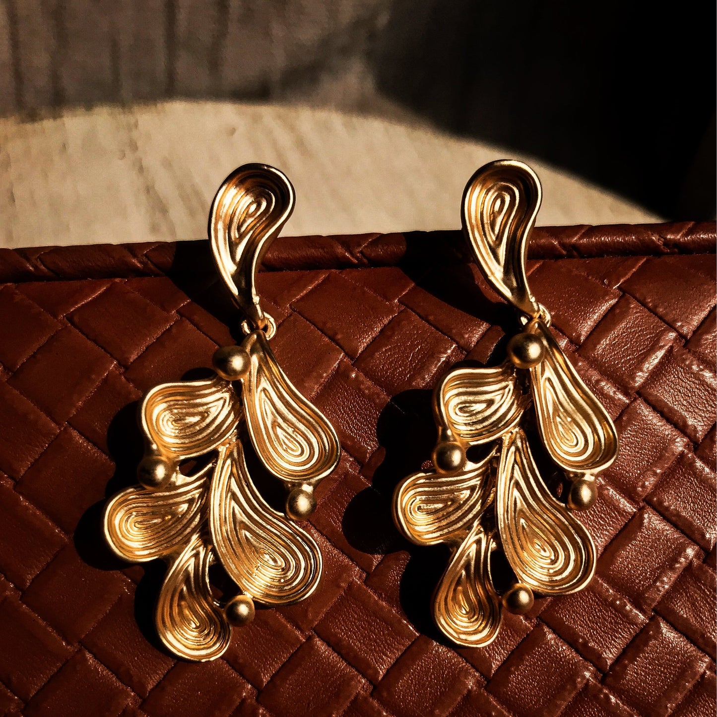 Two abstract drop earrings with swirling lines and small round accents, shown in silver, gold, rose gold, and black variations.