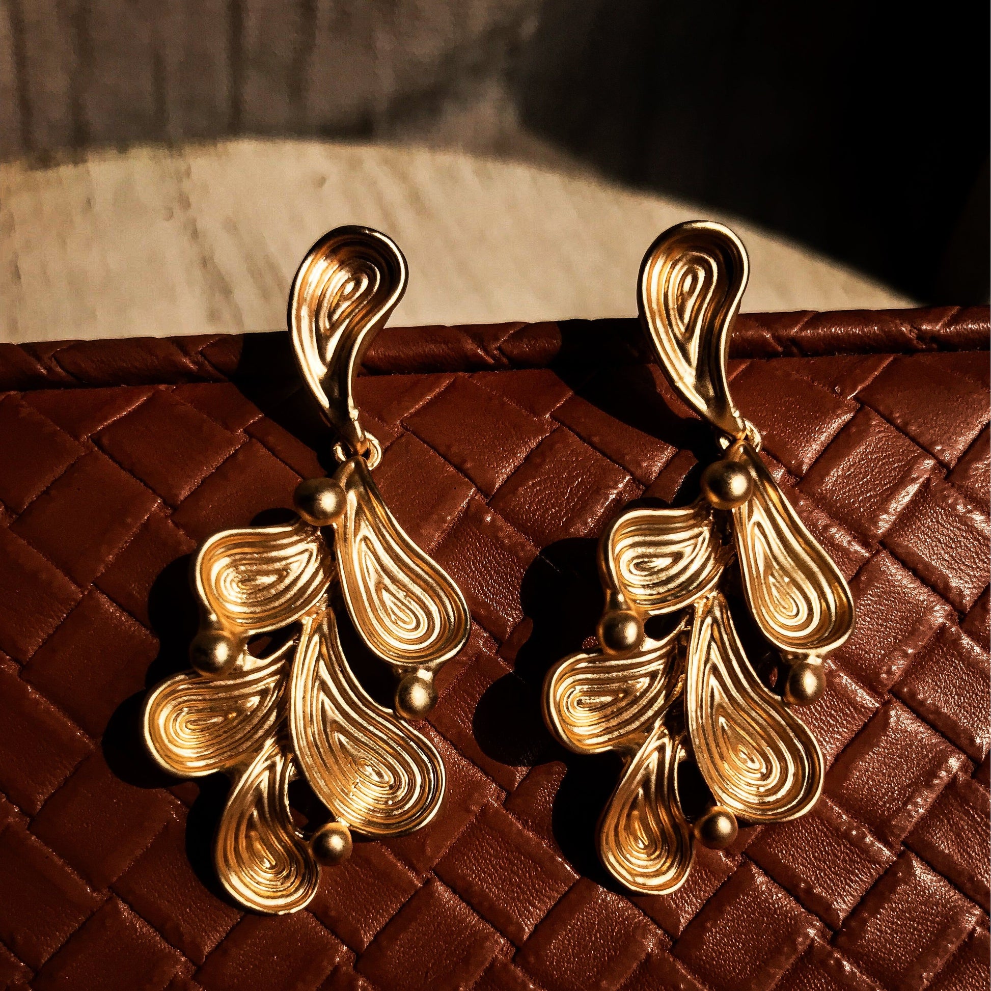 Two abstract drop earrings with swirling lines and small round accents, shown in silver, gold, rose gold, and black variations.