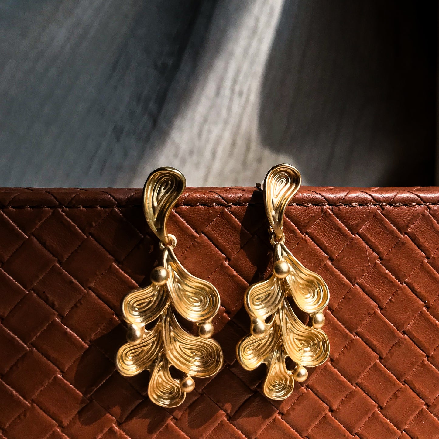 Two abstract drop earrings with swirling lines and small round accents, shown in silver, gold, rose gold, and black variations.