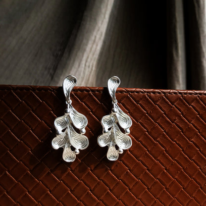 Two abstract drop earrings with swirling lines and small round accents, shown in silver, gold, rose gold, and black variations.