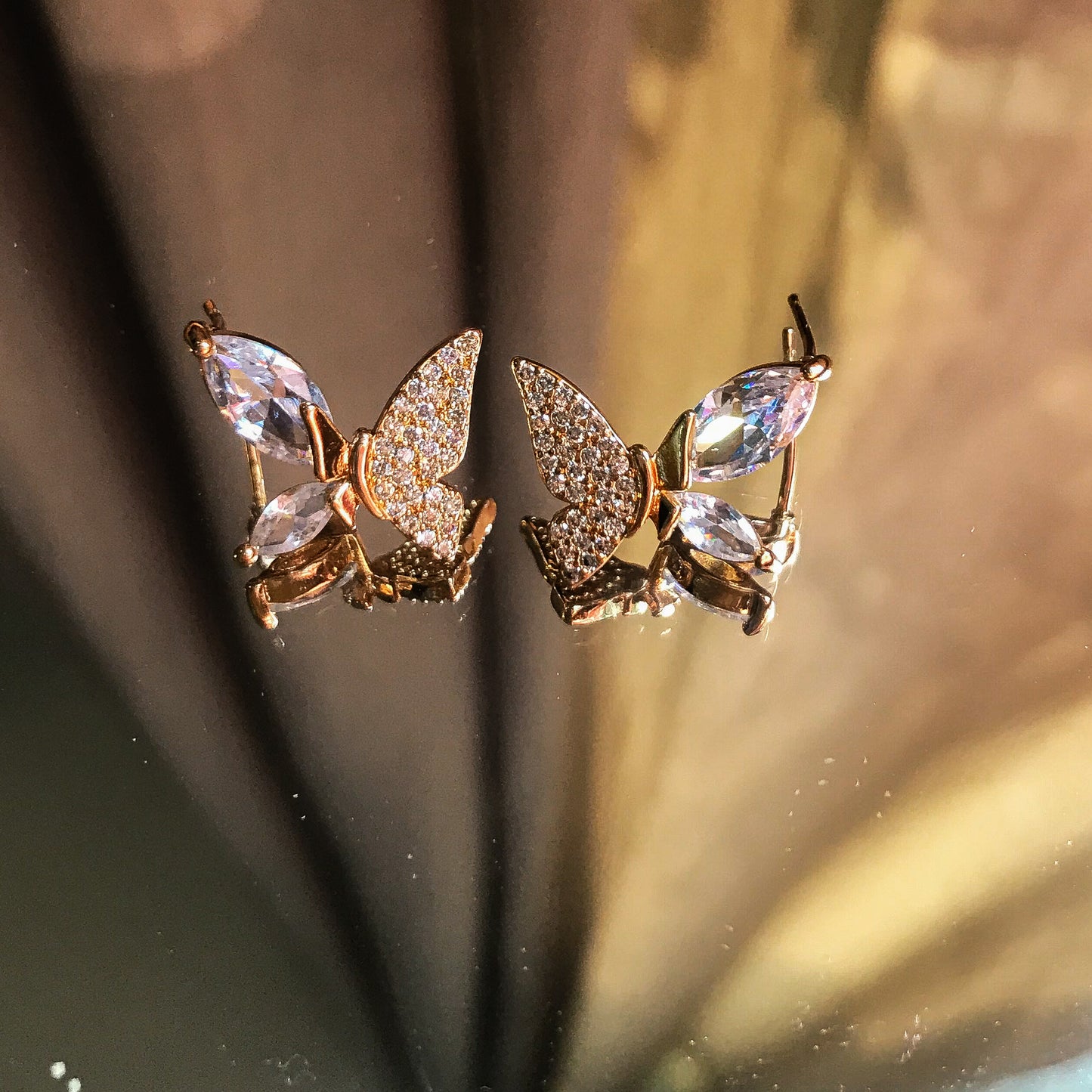 Two butterfly-shaped stud earrings, one silver and one gold, with marquise-cut stones forming the wing edges and smaller stones filling the inner wings, displayed on a reflective surface.
