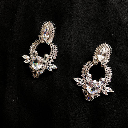 Two ornate silver-tone drop earrings featuring multiple clear marquise and oval-shaped sparkling stones, displayed against a black background.