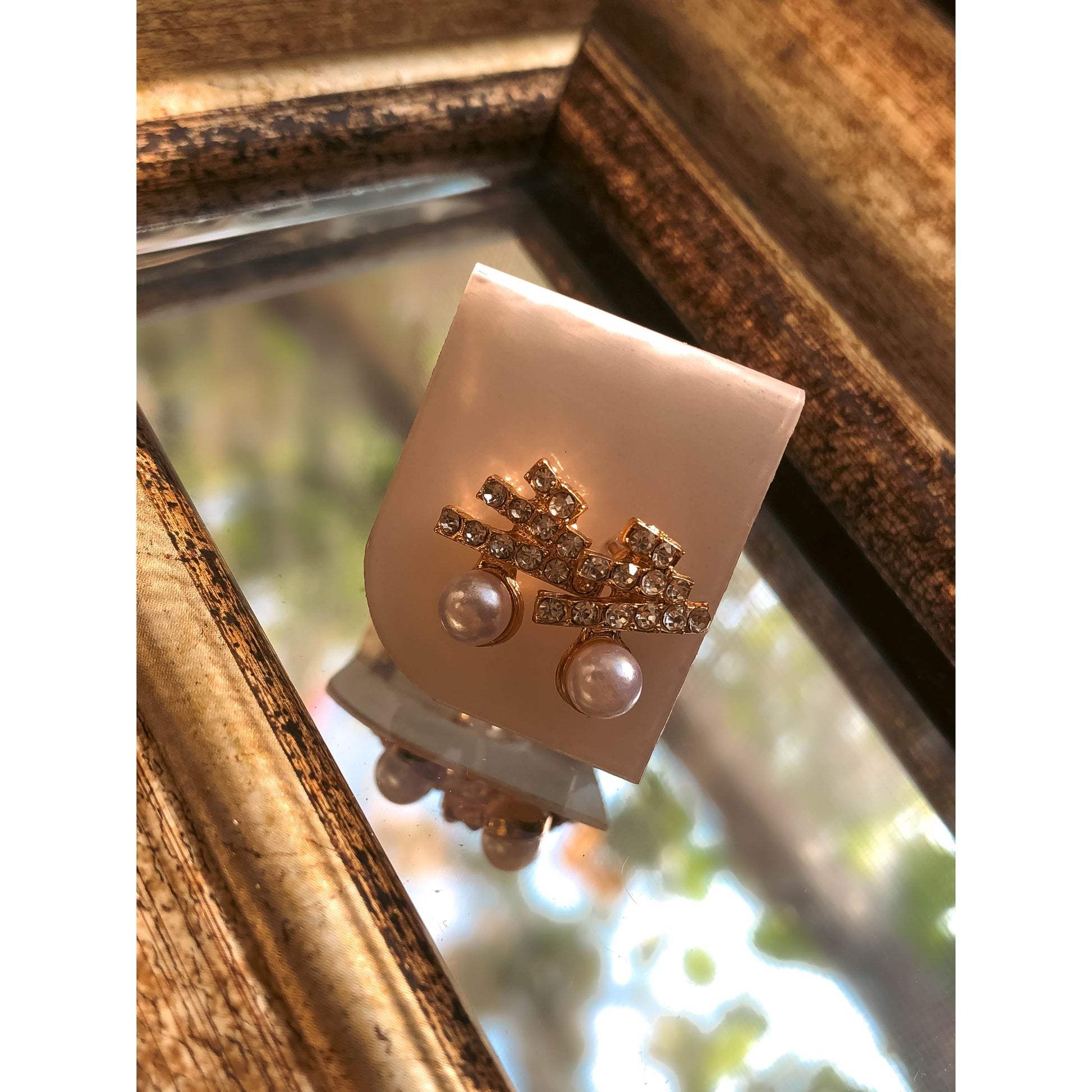 Two gold-tone drop earrings, each featuring a cluster of clear sparkling stones above a dangling white pearl, displayed on a light-colored earring card.