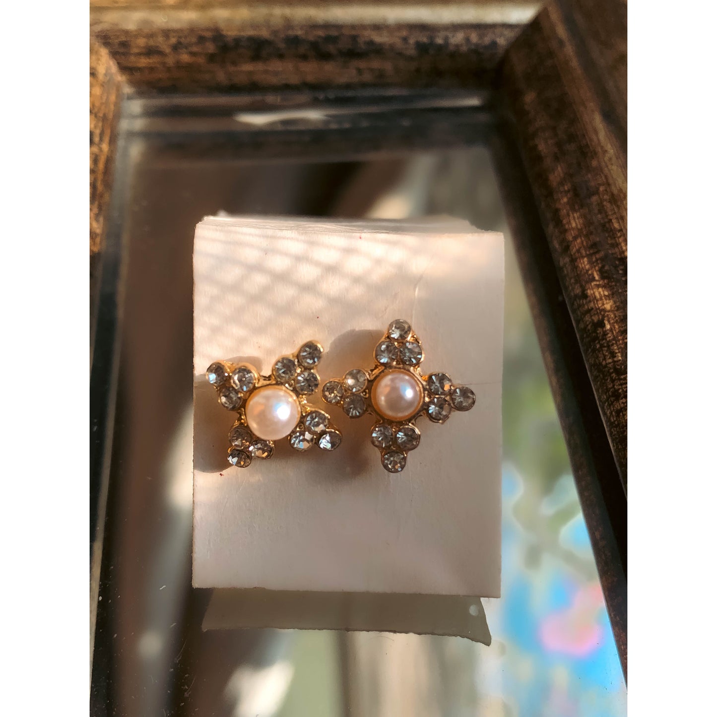 Two gold-tone stud earrings in the shape of stars, each with a white pearl in the center and sparkling clear stones on the star's points, displayed on a light-colored earring card.