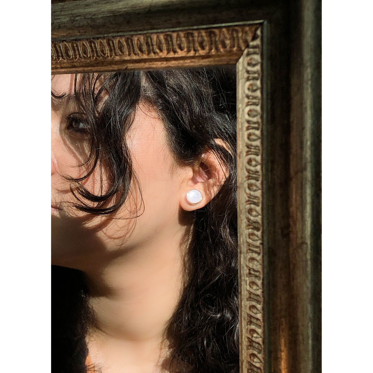A close-up of a golden-tone, ornate round stud earring with intricate filigree patterns