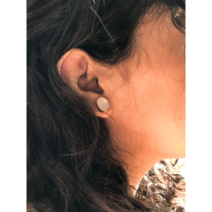 A close-up of a golden-tone, ornate round stud earring with intricate filigree patterns