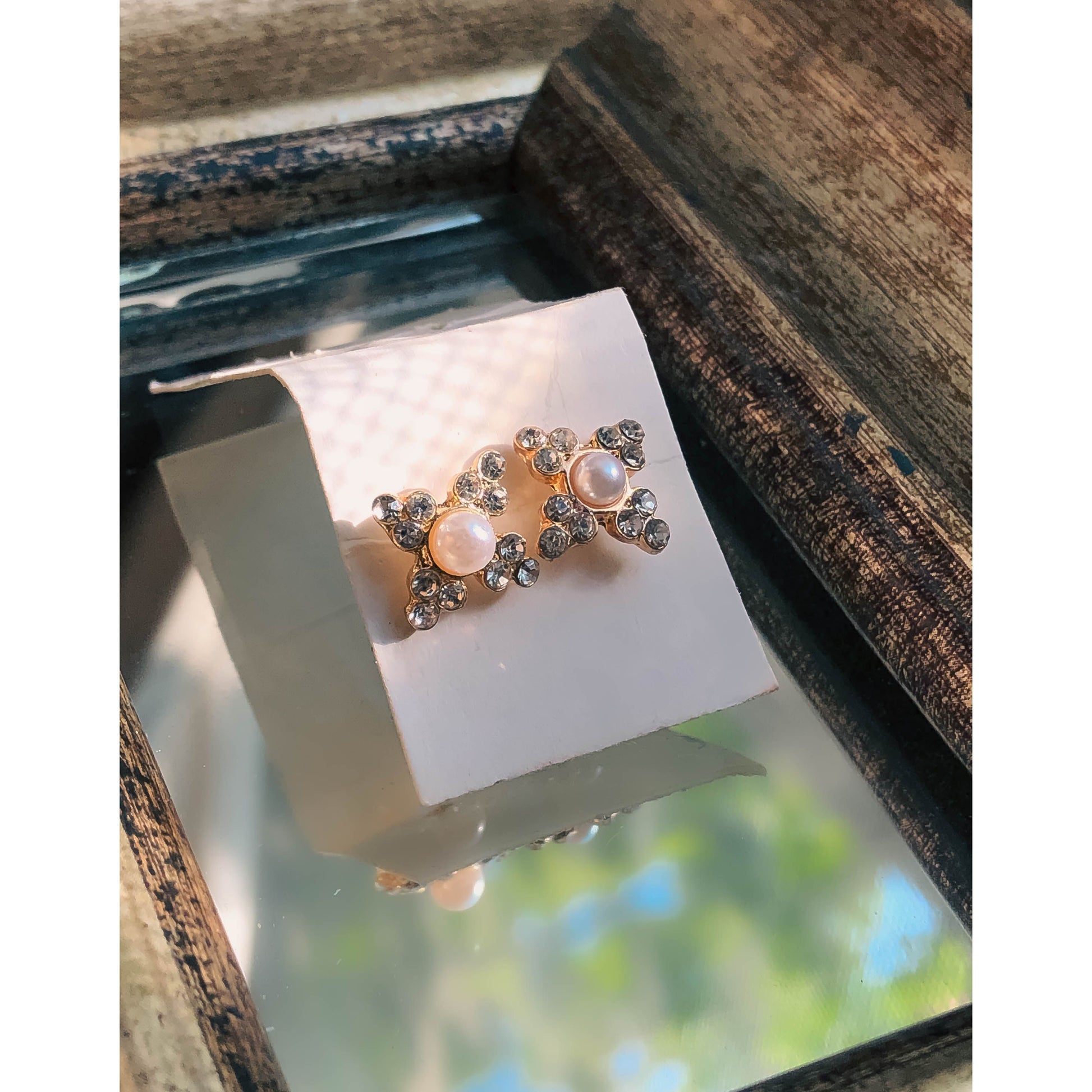 Two gold-tone stud earrings in the shape of stars, each with a white pearl in the center and sparkling clear stones on the star's points, displayed on a light-colored earring card.