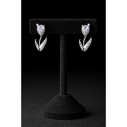 Silver tulip-shaped drop earrings with soft lavender crystal stones and pavé leaf detailing displayed on a black velvet T-bar stand against a dark black background in high-definition