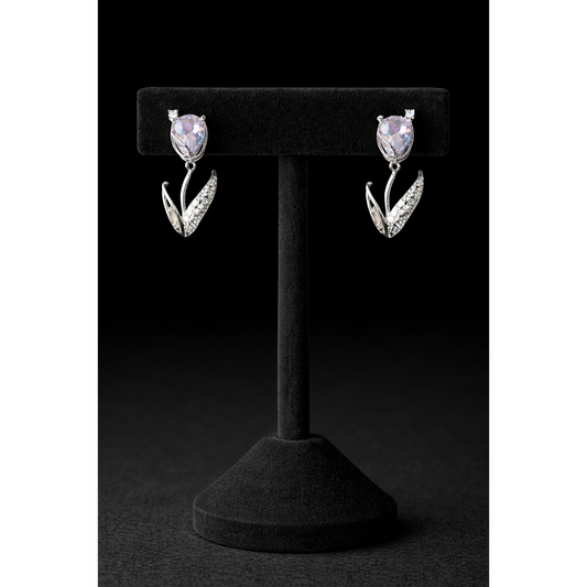 Silver tulip-shaped drop earrings with soft lavender crystal stones and pavé leaf detailing displayed on a black velvet T-bar stand against a dark black background in high-definition