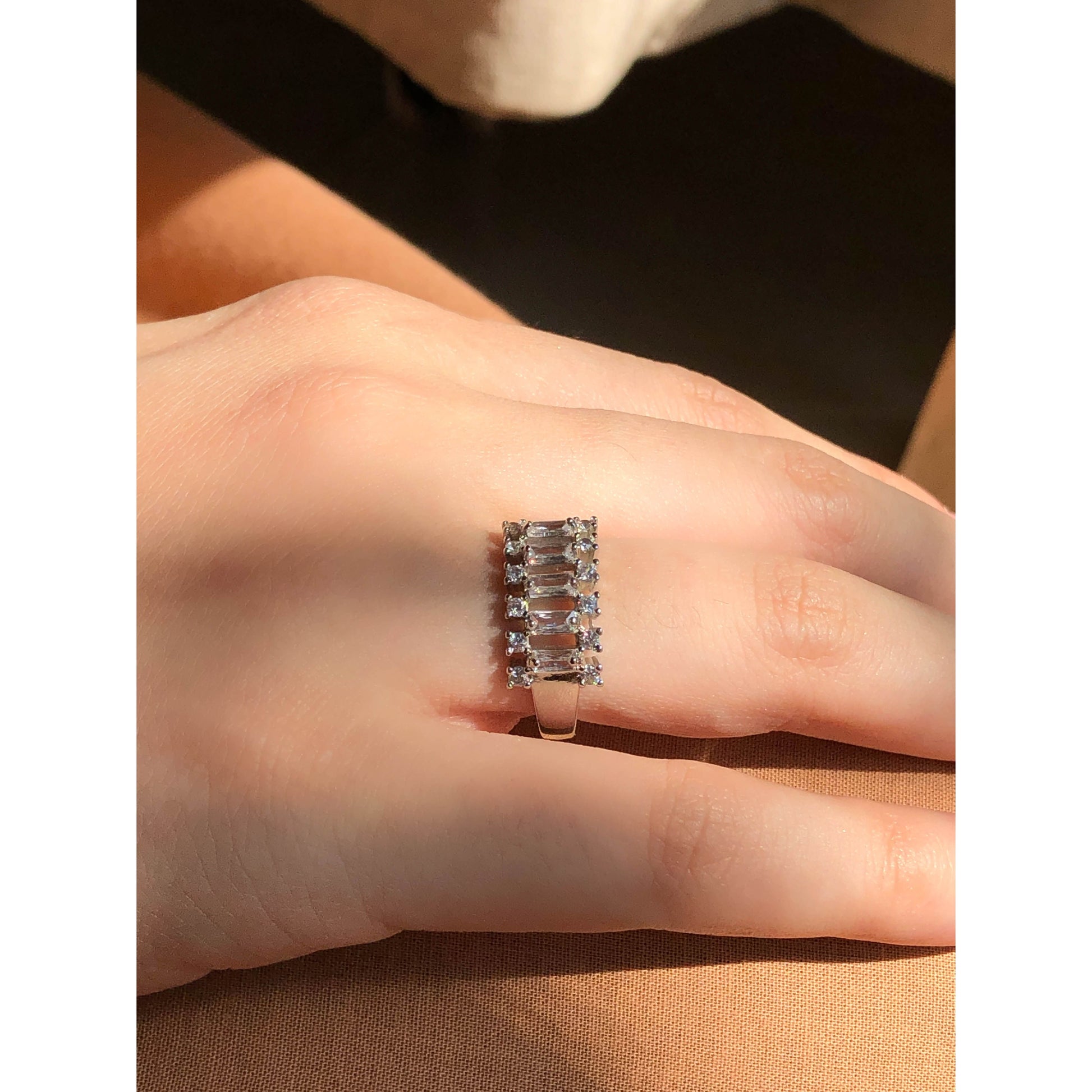 A close-up of a glittering ring featuring a large central clear stone and a band entirely covered in multiple rows of smaller clear sparkling stones.