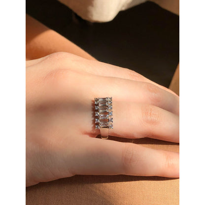A close-up of a glittering ring featuring a large central clear stone and a band entirely covered in multiple rows of smaller clear sparkling stones.