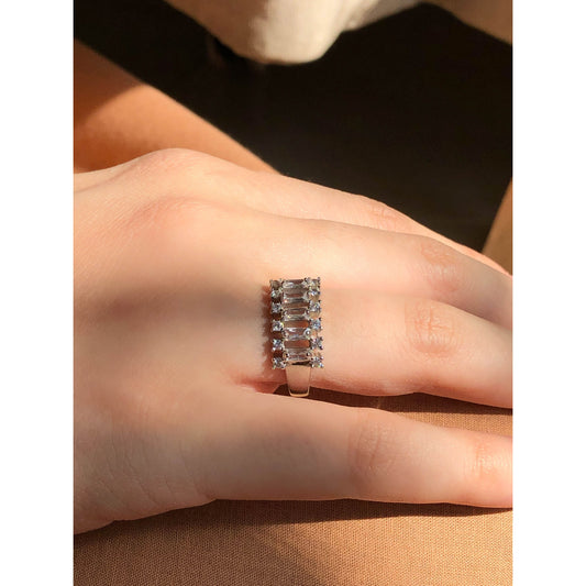 A close-up of a glittering ring featuring a large central clear stone and a band entirely covered in multiple rows of smaller clear sparkling stones.