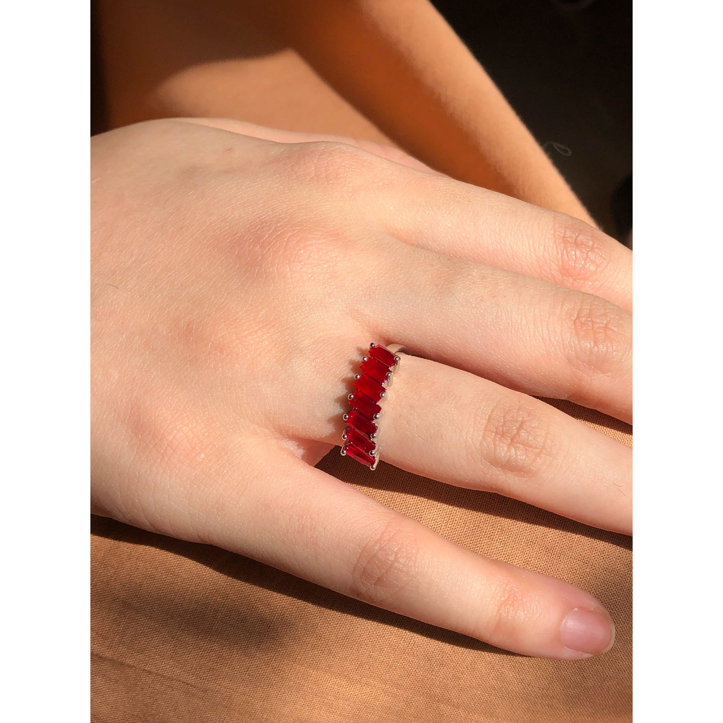 A close-up of a sparkling silver-tone ring featuring a large, rectangular emerald-cut clear stone in the center, flanked by smaller clear round stones set along the band.