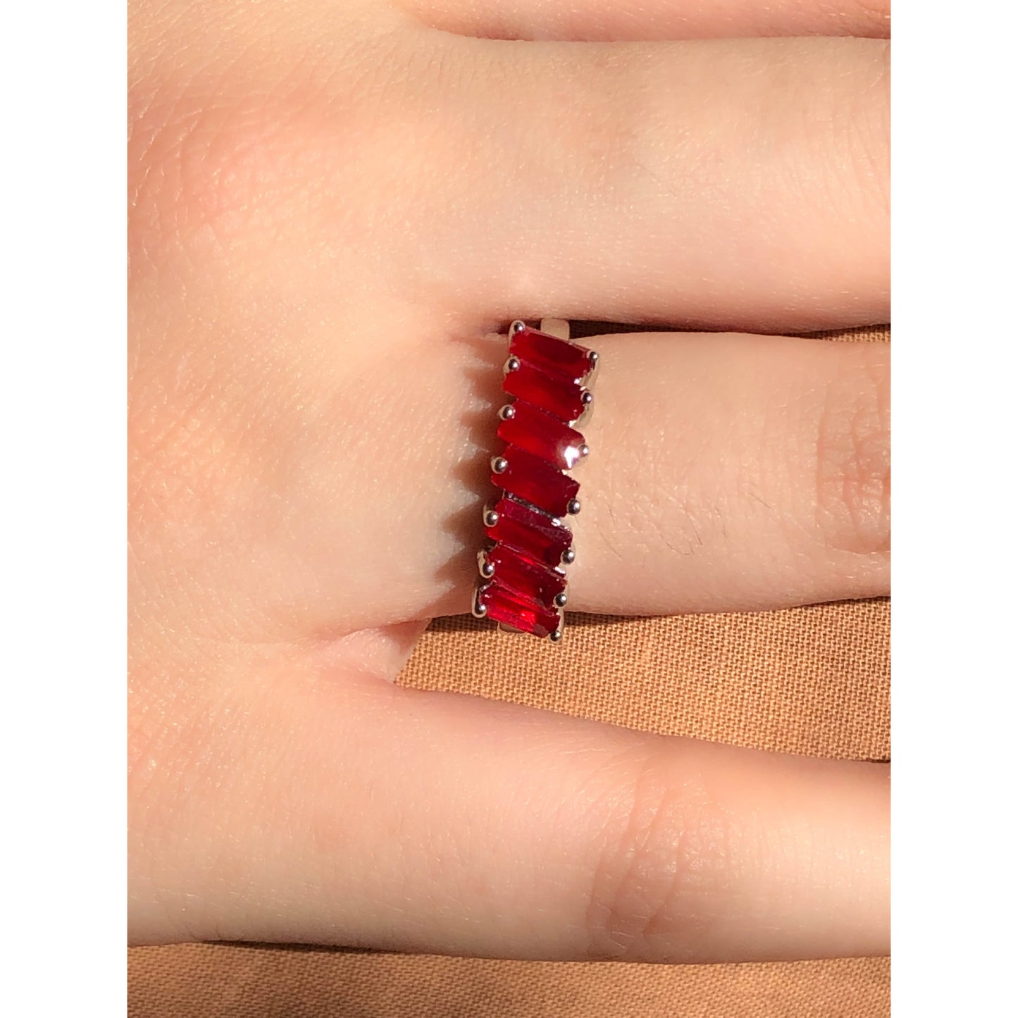 A close-up of a sparkling silver-tone ring featuring a large, rectangular emerald-cut clear stone in the center, flanked by smaller clear round stones set along the band.