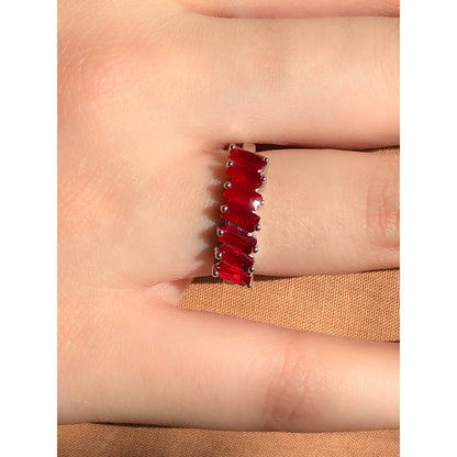 A close-up of a sparkling silver-tone ring featuring a large, rectangular emerald-cut clear stone in the center, flanked by smaller clear round stones set along the band.
