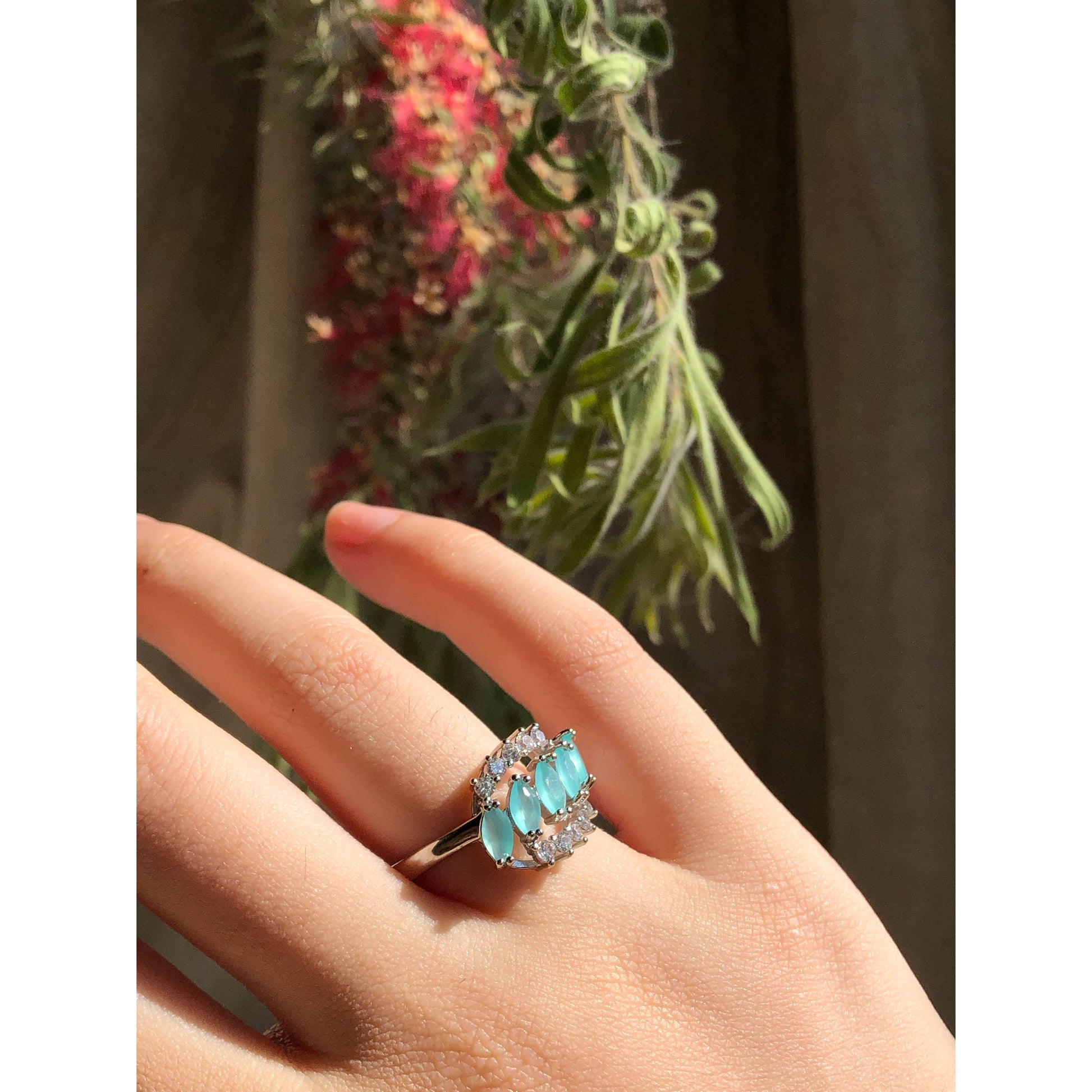 A close-up of a sparkling silver-tone ring featuring a large round clear stone surrounded by a halo of smaller clear stones, with more small clear stones set along the band.
