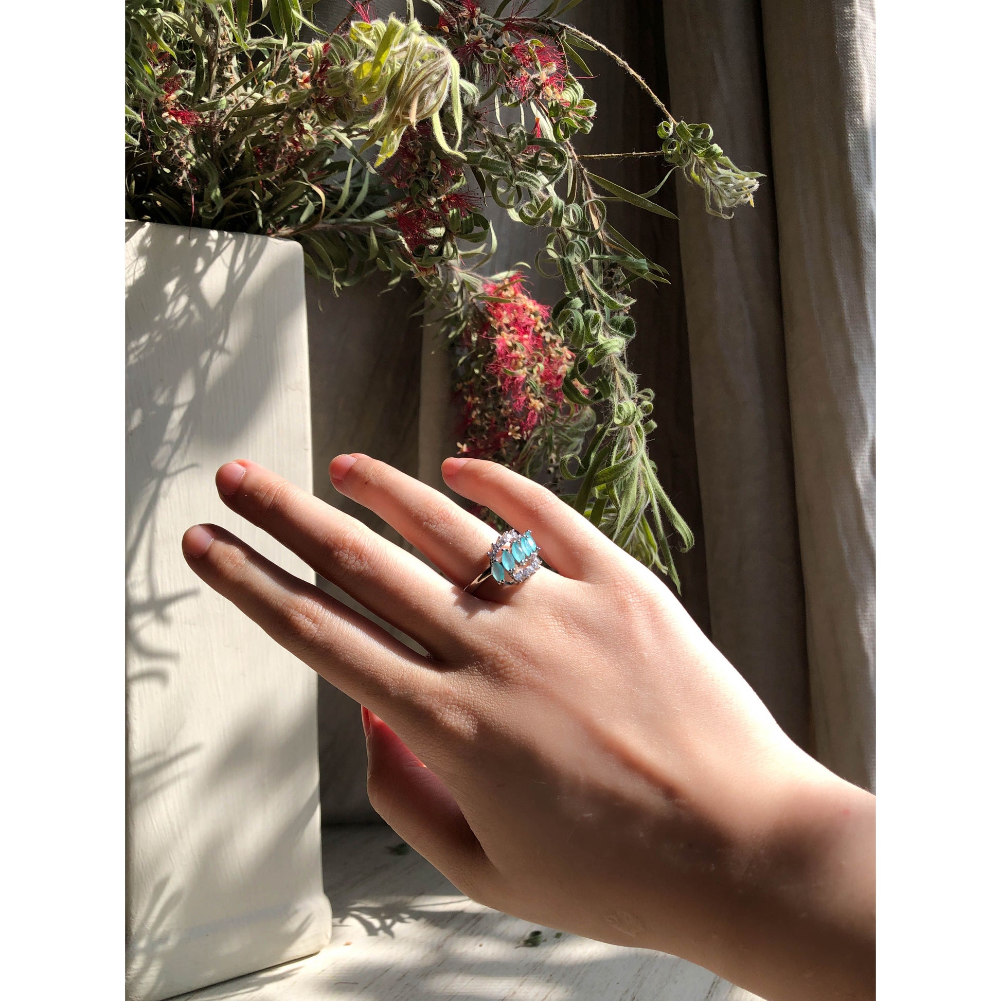A close-up of a sparkling silver-tone ring featuring a large round clear stone surrounded by a halo of smaller clear stones, with more small clear stones set along the band.