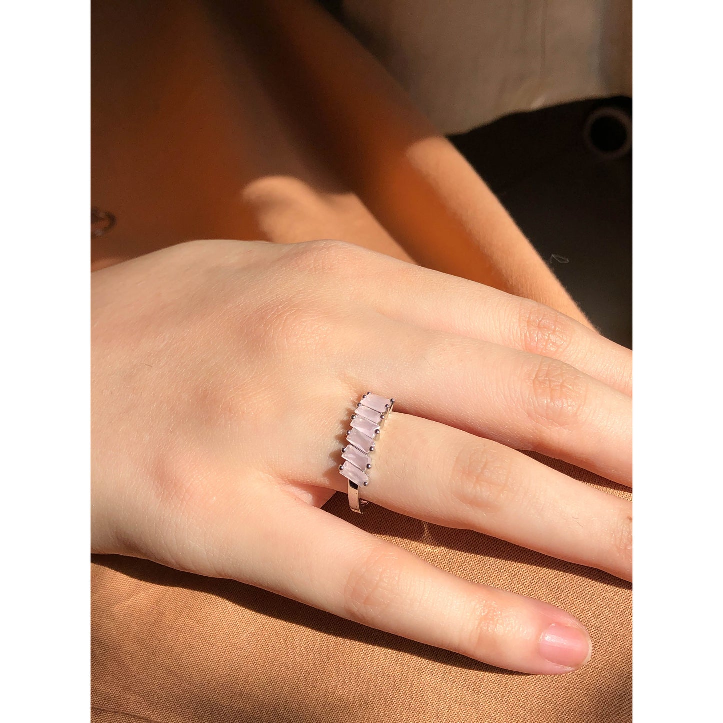 A close-up of a sparkling silver-tone ring featuring a large, rectangular emerald-cut clear stone in the center, flanked by smaller clear round stones set along the band.
