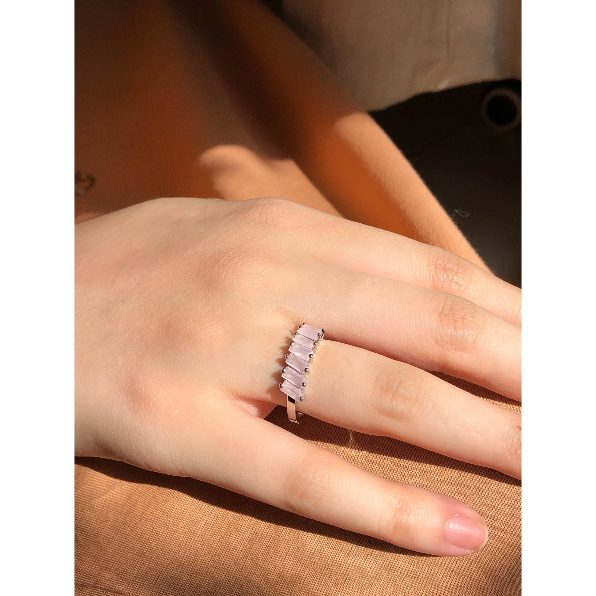 A close-up of a sparkling silver-tone ring featuring a large, rectangular emerald-cut clear stone in the center, flanked by smaller clear round stones set along the band.