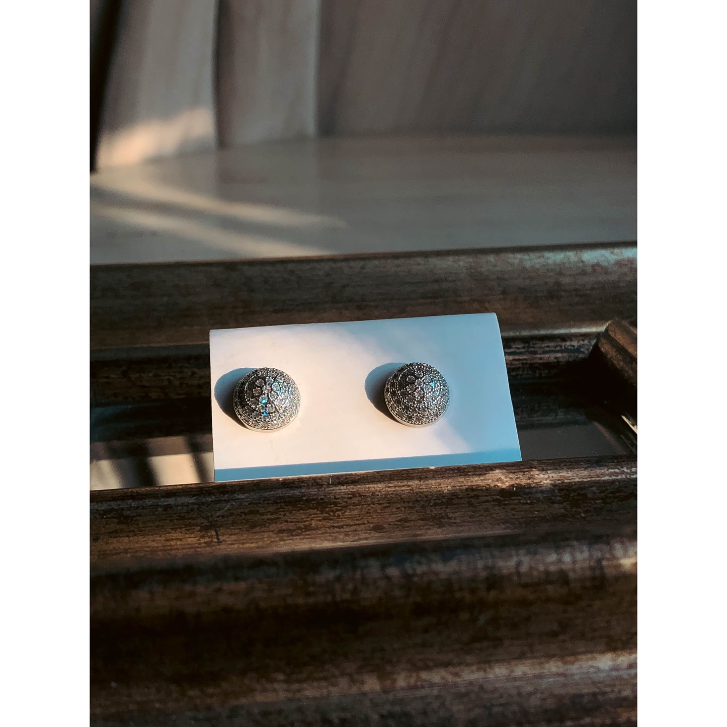 A close-up of a silver-tone, round, dome-shaped stud earring completely covered in small, clear, sparkling stones