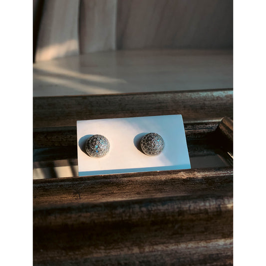 A close-up of a silver-tone, round, dome-shaped stud earring completely covered in small, clear, sparkling stones