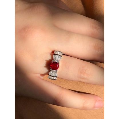 A silver-tone ring featuring an oval-cut gemstone in aqua and blush options, accented by stacked baguette-cut crystals on each side, worn on a hand with warm-toned fabric in the background.