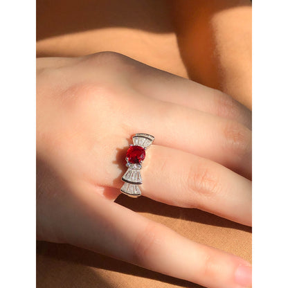 A silver-tone ring featuring an oval-cut gemstone in aqua and blush options, accented by stacked baguette-cut crystals on each side, worn on a hand with warm-toned fabric in the background.