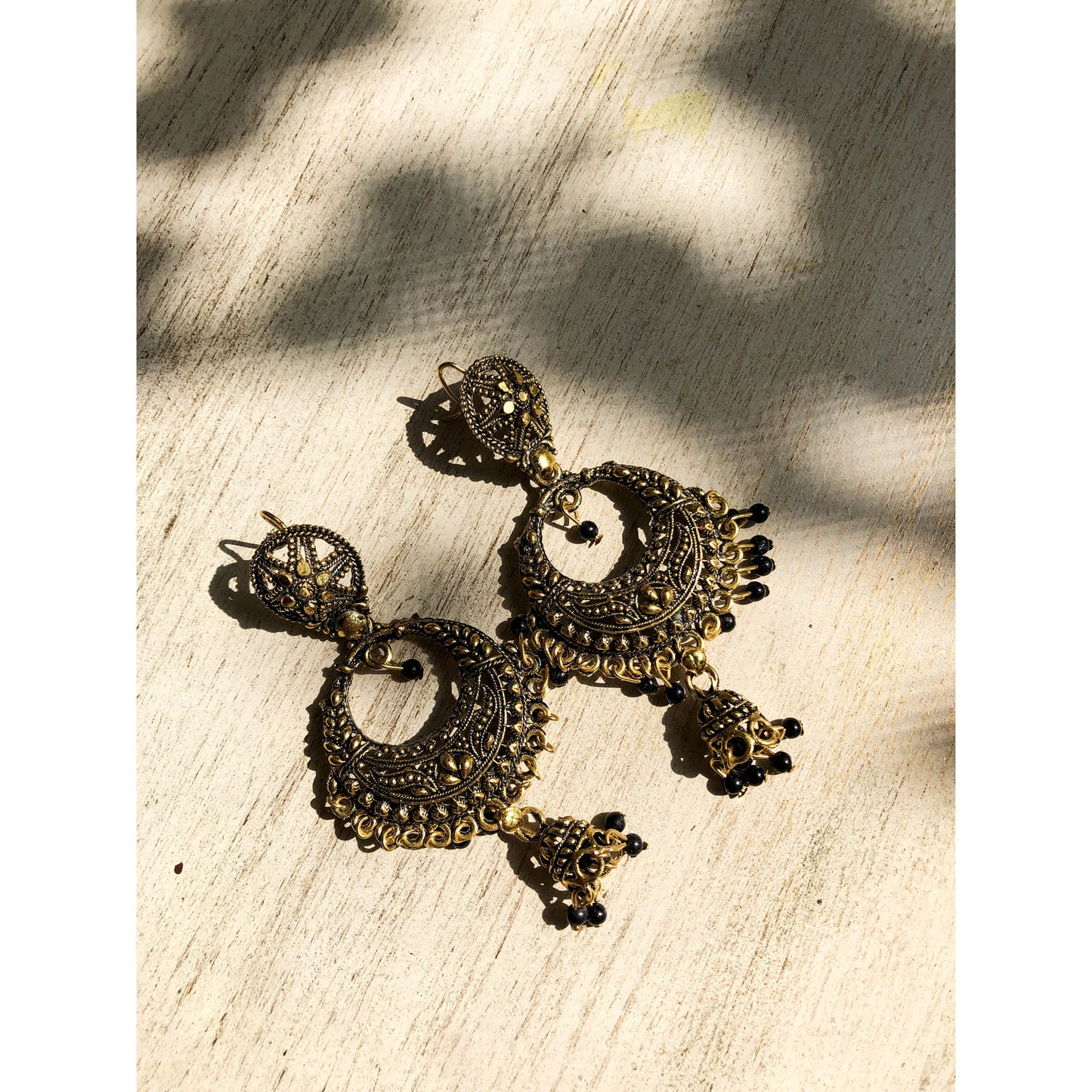 A collection of traditional jhumka earrings, featuring ornate bell shapes with intricate filigree details and various colorful accents like blue enamel or small dangling beads.